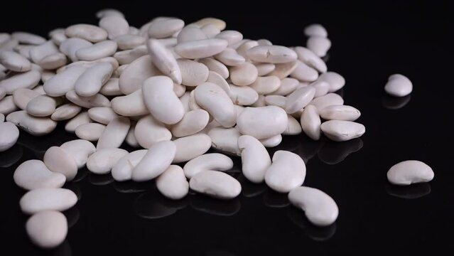 White beans cascading in slow motion onto a reflective black surface, poured from glass containers, perfect for vegan dishes.
