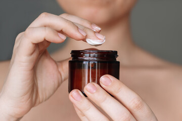 Cropped shot of a young woman taking moisturizing cream with her finger holding brown glass...