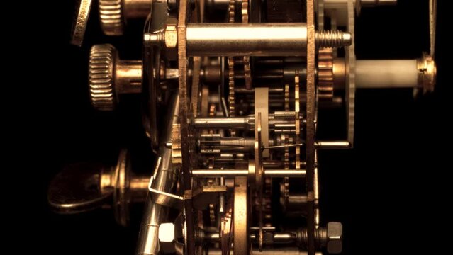 clockwork mechanism of an old ALARM CLOCK  disassembled with golden cogwheels running on silver steel closeup gear movement working close-up side view detail swiss made antique watch isolated on black