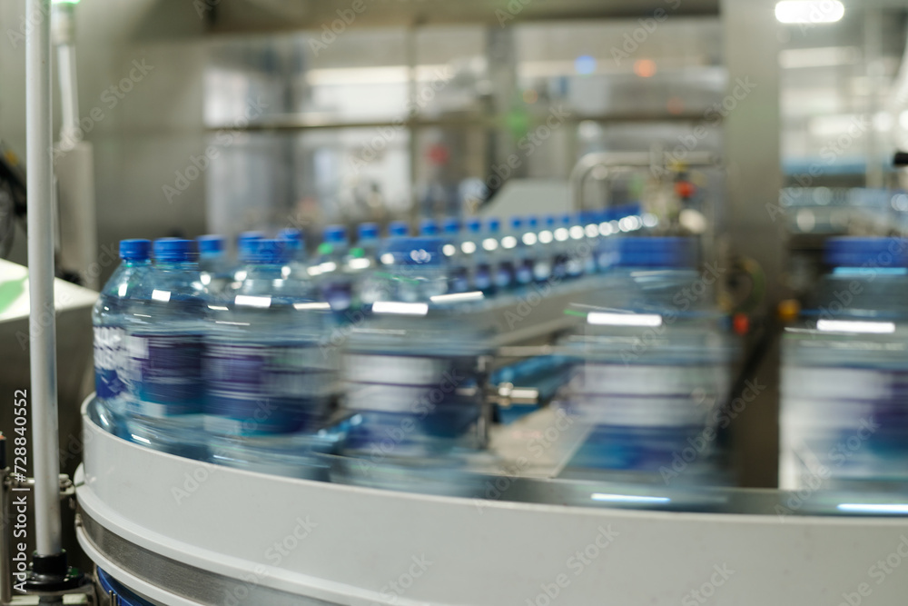 Aufkleber part of moving production line with capped plastic bottles containing mineral water or some other dr