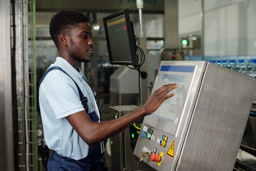 Naklejka na ściany i meble Young African American worker standing in front of display of factory equipment or automated production line and entering data