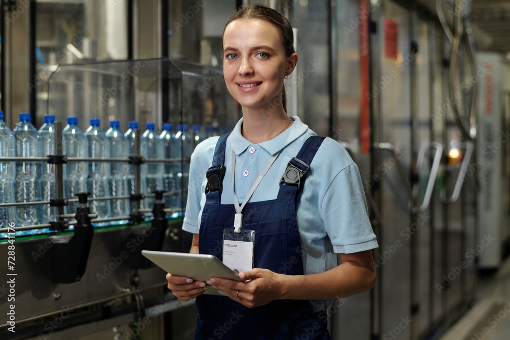 Poster young successful engineer or inspector with tablet looking at camera while standing in industrial pl