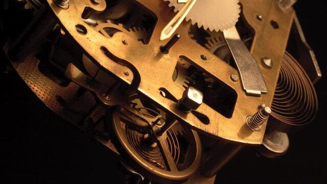 clockwork mechanism of an old ALARM CLOCK  disassembled with golden cogwheels running slowly on silver steel hands gear movement working closeup low angle shot detail antique watch isolated on black