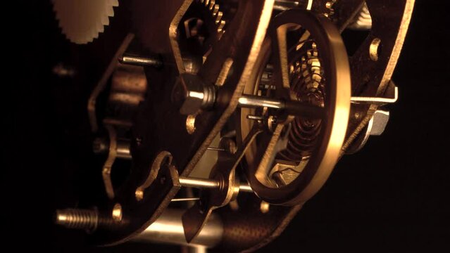 clockwork mechanism of an old ALARM CLOCK  disassembled with golden cogwheel running slowly on silver steel close-up gear movement working closeup low angle shot detail antique watch isolated on black