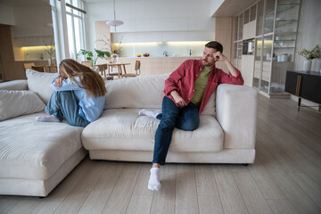 Obraz premium Indifferent uncaring man abuser with dissatisfied look sitting on sofa, neglecting wife, while offended upset desperate woman crying after quarrel, argue, disagreement. Family crisis, gaslighting