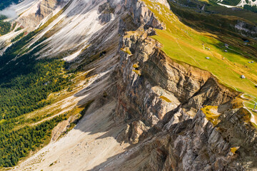 Rocky Seceda ridgeline against green valley and forests in Italian Alps. Light haze hovers over highland on summer day aerial view