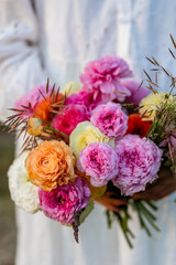 Beautiful bright colourful bridal wedding bouquet with fresh ranunculi flowers. Bride in a white lace dress. Sunset light