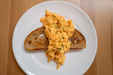 Scrambled egg served across a slice of buttered sourdough toast on a white plate. - 728845324