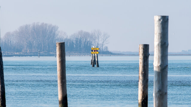 Grado, Italy - January 28th, 2024: Maritime directions to Trieste or the Barbana Sanctuary. Signs hanging in the middle of the navigable canal in the lagoon. Foggy day.