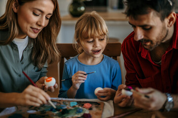 Fototapeta premium Parents and daughter share laughs while decorating Easter eggs