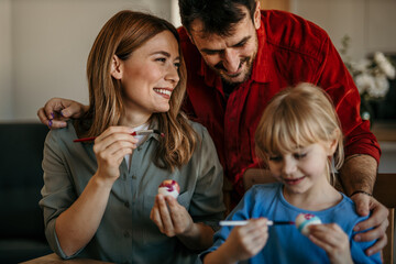 Mom, dad, and daughter engage in joyful egg decorating festivities