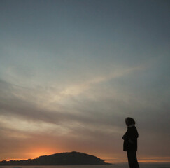 A girl on the beach contemplates the sunset, the sea and the mountain in the background. 