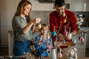 Mom, dad, and daughter happily decorating Easter eggs in their dining room