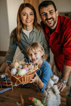 Happy family of three gathered around an Easter table, joyfully decorating colorful eggs
