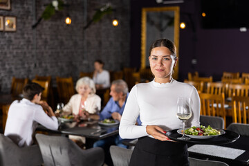 Smiling, positive waitress woman holds tray with order in hand and invites new visitors to pass...