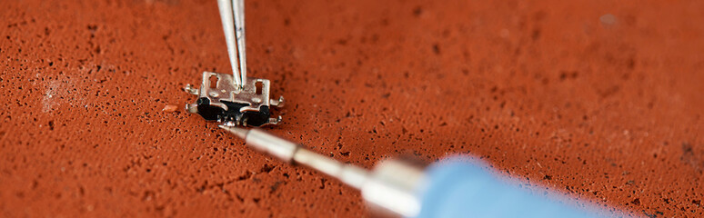 close up view of tweezers and soldering iron near electronic chipset on table in repair shop, banner