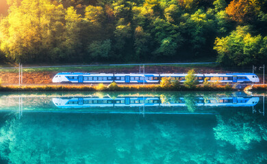 Beautiful blue modern high speed train and river in alpine mountains at sunrise in spring....