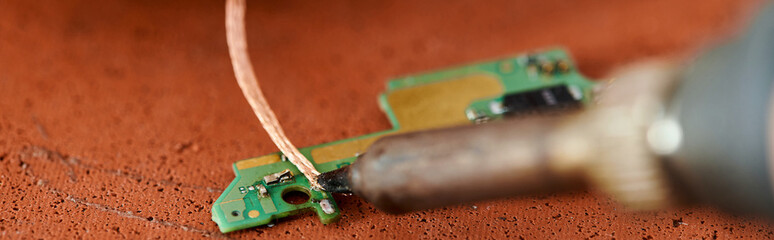 soldering iron near microscheme of electronic device on table in repair workshop, horizontal banner