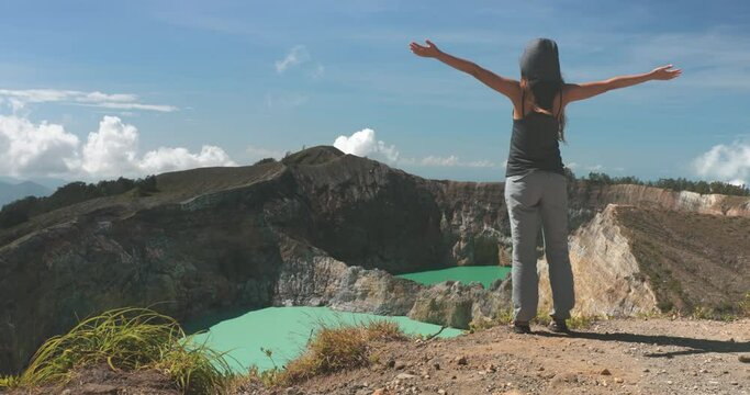 Woman raise hands on volcano mountain crater edge. Volcanic Kelimutu blue crater lakes. Travel destination. Beautiful wild landscape. Female tourist on summer vacation. Lifestyle holiday concept