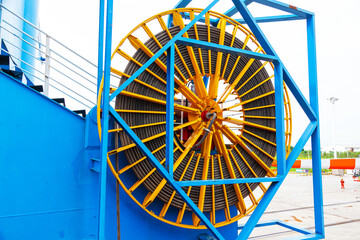 A large wheel with a harbor crane electric cable coiled around it in the port area.