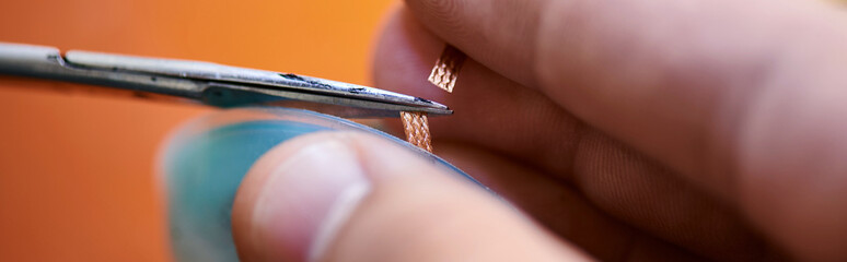 partial view of experienced technician cutting wire of electronic device in repair shop, banner