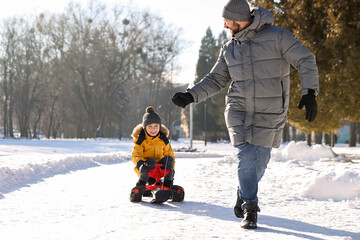 Family time. Father pulling his happy son on sledge in snowy park. Space for text