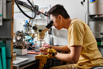 side view of professional asian specialist with microscope examining electronic device in workshop