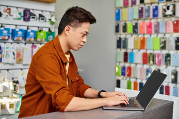 concentrated asian man using laptop on counter in private electronics shop, small business concept