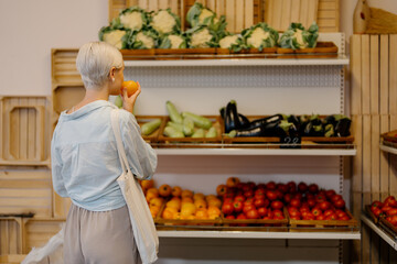 Woman inspects the aroma of a yellow tomato at an indoor fresh produce market