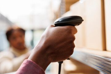 African american warehouse worker hand holding barcode scanner and doing goods inventory. Retail storehouse employee arm scanning cardboard box to check package code close up