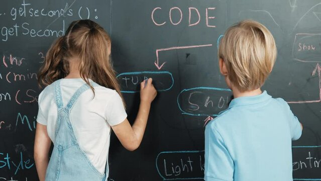 Caucasian girl writing blackboard with engineering prompt or coding, programing system written in STEM technology classroom and turnaround to looking at camera while boy showing thumb. Erudition.