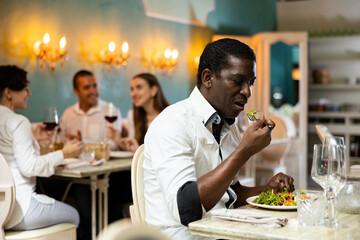 Single man eating salad at the restaurant with a group of young people on the background