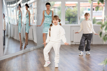 Cute preteen girl rehearsing famous funny Charlie Chaplin walk in mirrored choreography studio during dance class led by female instructor ..