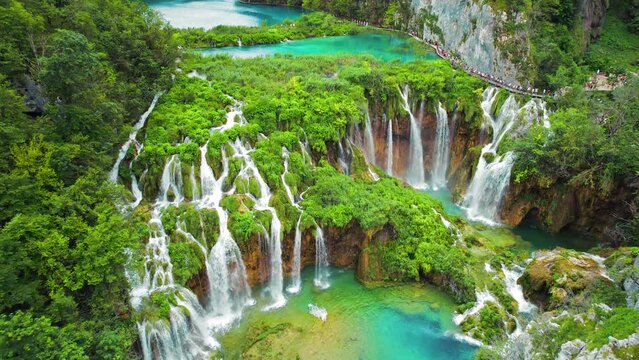 Crowd of tourists visit famous Plitvice waterfalls in Croatia. Mountain streams flow into a lake with azure clear water.