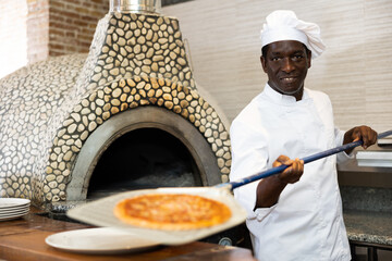 Portrait of happy chef getting ready pizza out of oven in restaurant kitchen