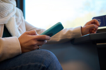 Close-up female hand holding smartphone, checking mobile app, planning route while travelling by comfortable city train