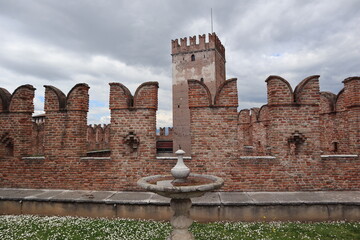 Picturesque fountain among green grass and blooming daisies in a fortress with red brick walls, Verona landmark, Old Castelvecchio castle