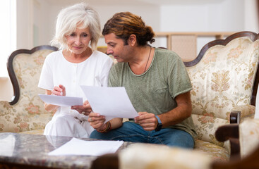 Aged woman and man doing paperwork together at home, reading and discussing documents - obrazy, fototapety, plakaty