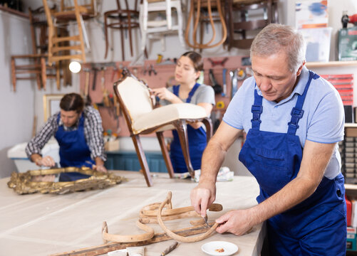 Mature male furniture workshop worker carving wooden vintage chair parts