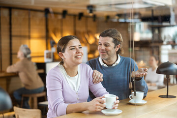 Fototapeta premium Joyful man and woman chatting while sitting at bar counter with a cup of coffee