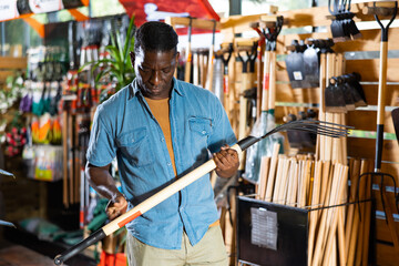 Focused adult african american man looking for pitchfork to work in his garden at gardening supply...