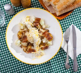 Top view of baked potatoes served with cauliflower, bacon and mushrooms with sauce and grated cheese on white plate..