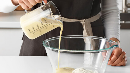Closeup of man using a glass measuring cup to pour mixture in bowl with flour.