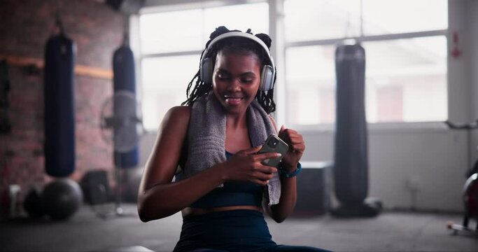 African woman, phone and headphones in gym for music with choice, chat and dancing at training. Person, smartphone and happy dancer with listening to audio streaming subscription with mobile app