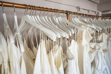 Color photo of luxury wedding dresses hanging on white hangers on a long rack at bridal boutique