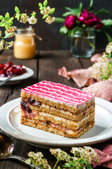 Piece of delicious biscuit cake with cherry and condensed milk on the plate over dark wooden background with berries and flowers. Sweets, dessert and pastry, homemade cakes, close up, selective focus