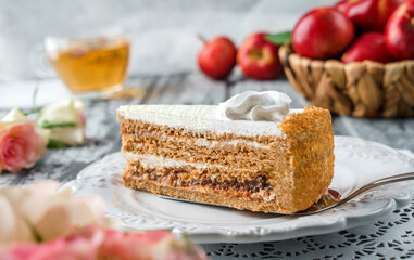Piece of delicious cake with cream and apple jam on the plate over grey background with fresh apples and flowers. Sweets, dessert and pastry, close up, selective focus