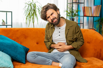 Middle eastern arabian man sits on sofa feeling sudden strong abdominal stomach ache gastritis...