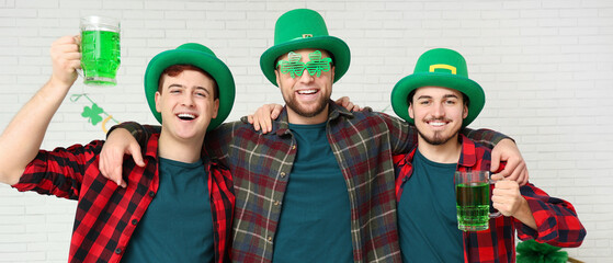 Happy young men with mugs of green beer on light background. St. Patrick's Day celebration