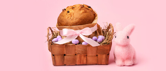 Basket with delicious Easter cake, painted eggs and bunny on pink background